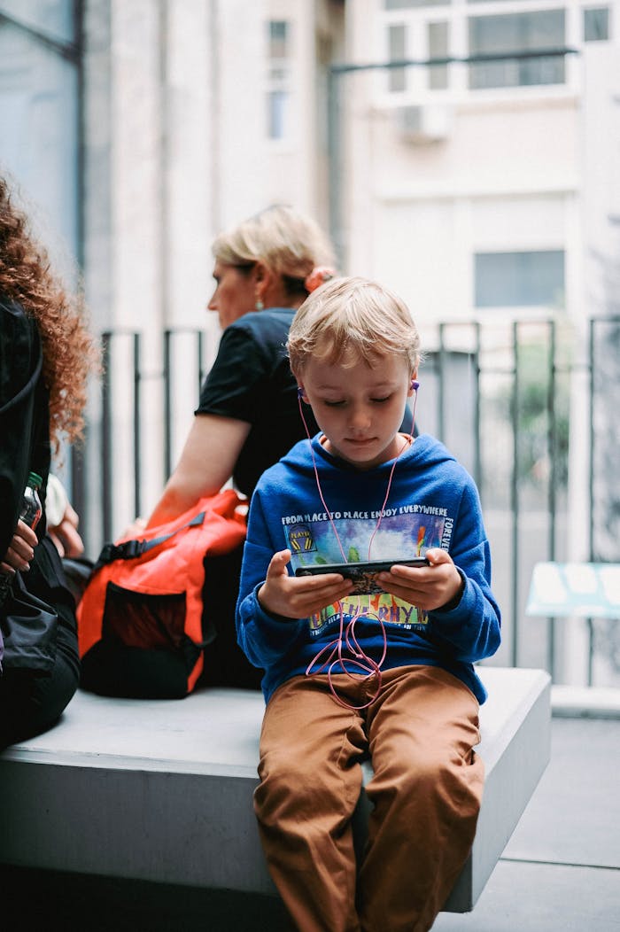 Young boy using a smartphone with headphones in a bustling urban environment.