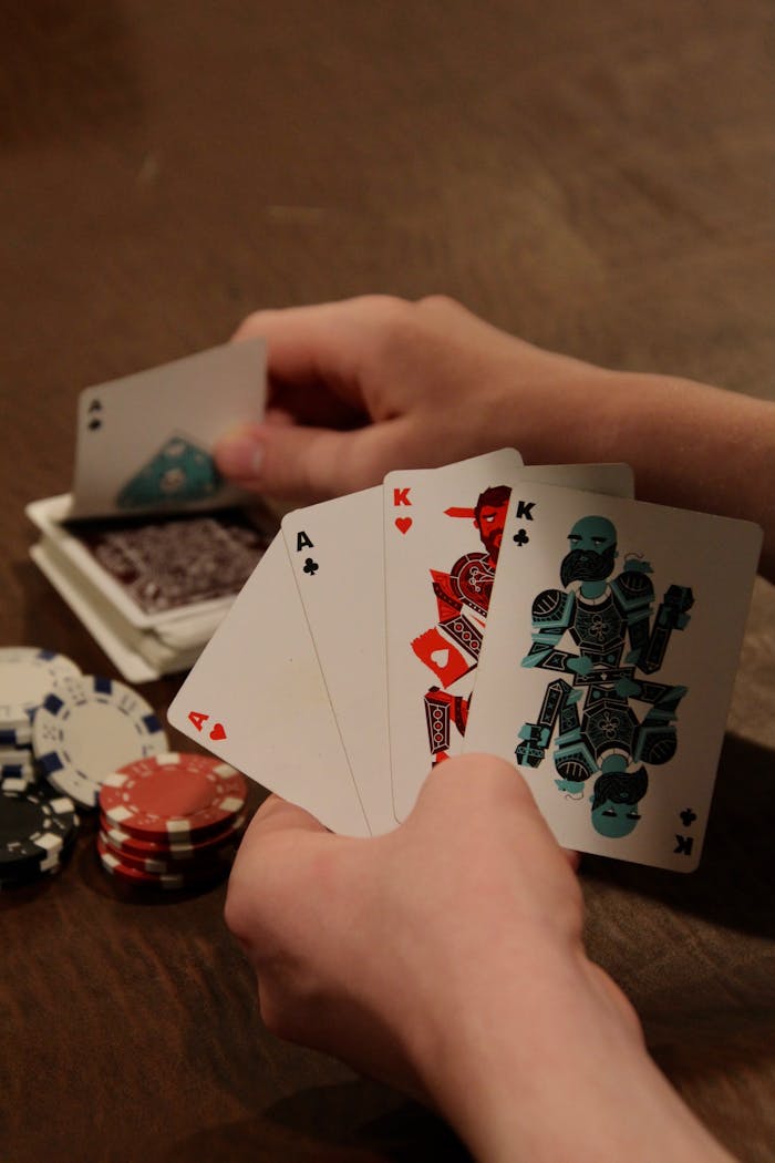 Close-up of hands holding aces and kings with poker chips on table.